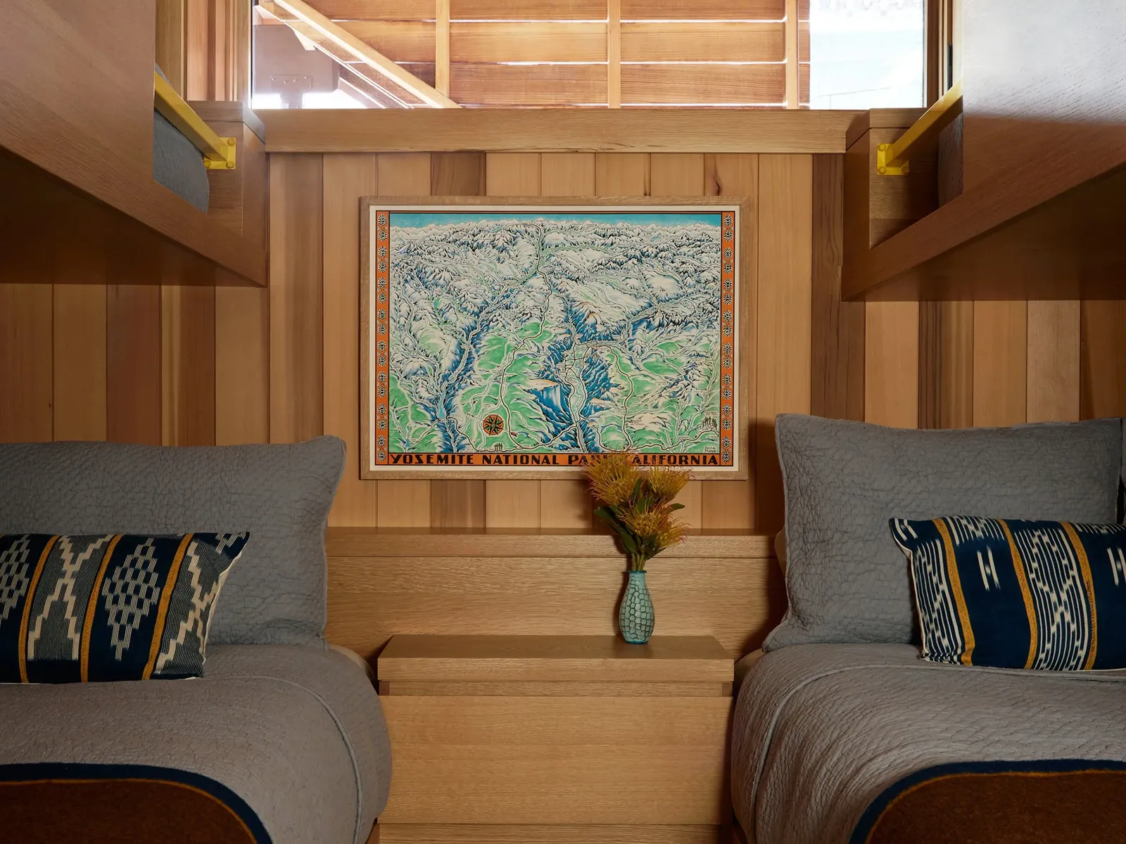 Pair of built-in oak bunk beds with grey quilts and indigo cushions, a vintage Yosemite map on the panelled wall between them.