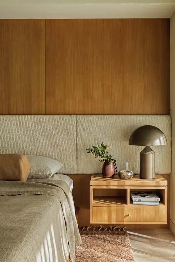 Bed against an upholstered wall-length headboard and oak panelling, a mushroom lamp on the floating oak nightstand.