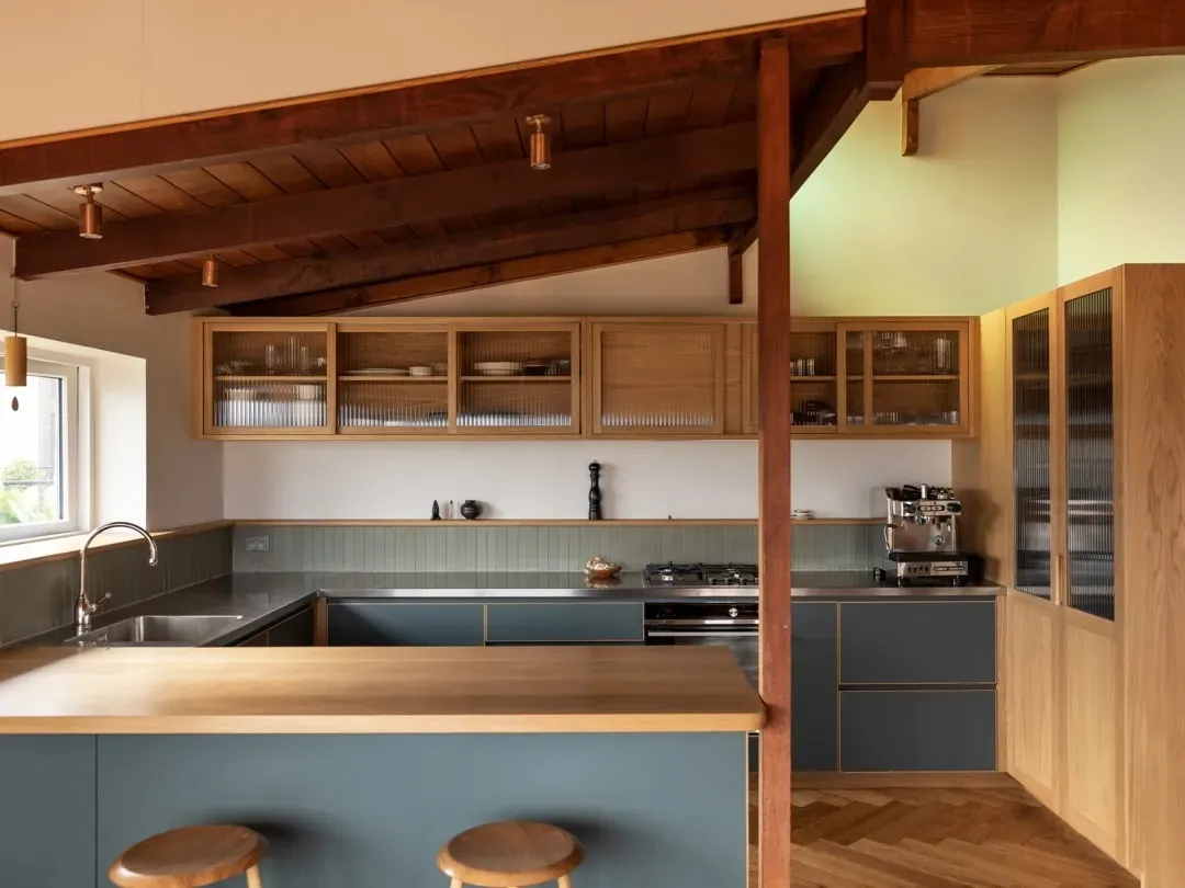Kitchen with blue-grey cabinets and an oak peninsula under exposed timber rafters, with reeded-glass upper cupboards.