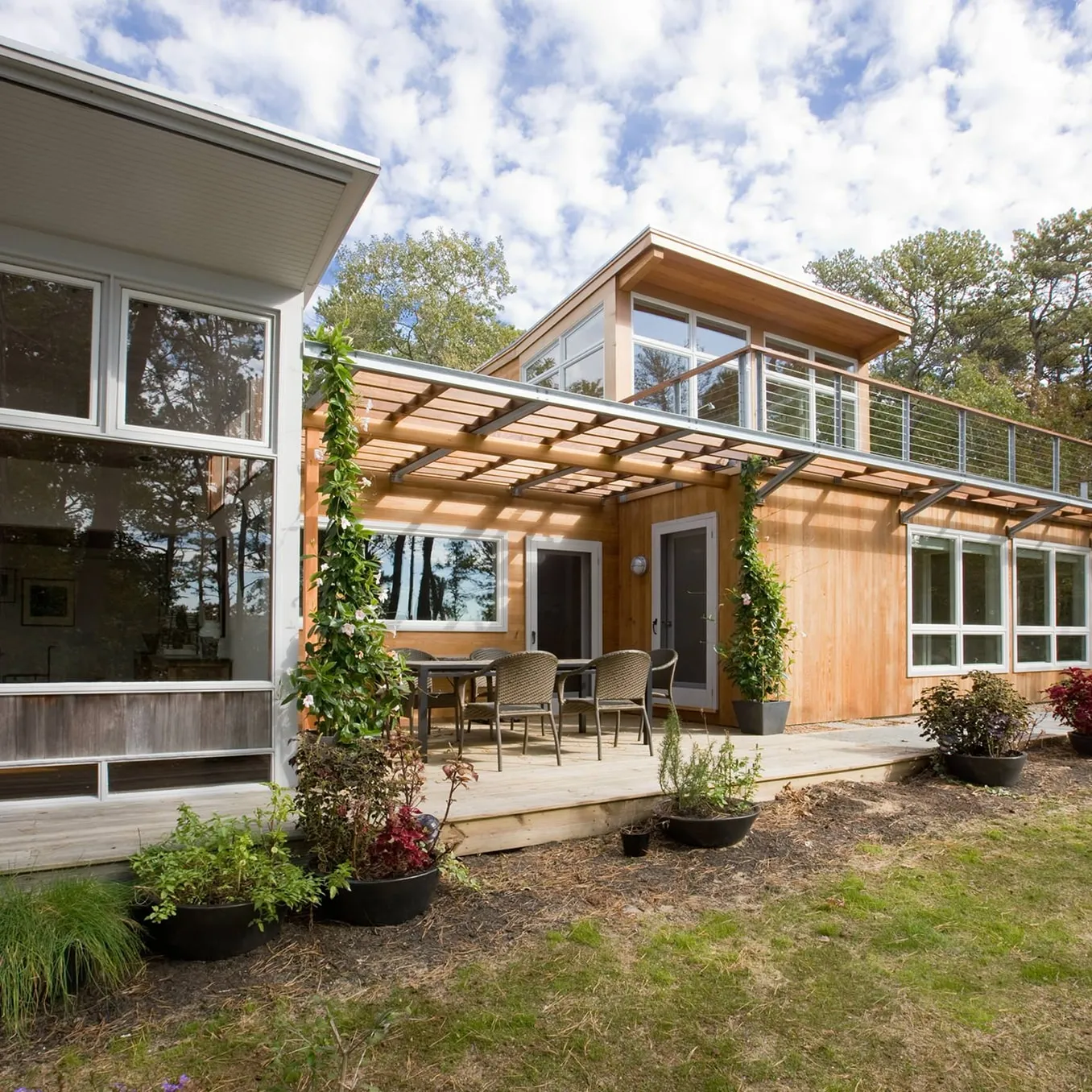 Cedar-clad addition with a clerestory upper storey and a pergola sheltering a dining deck, joined to the original white-framed house.